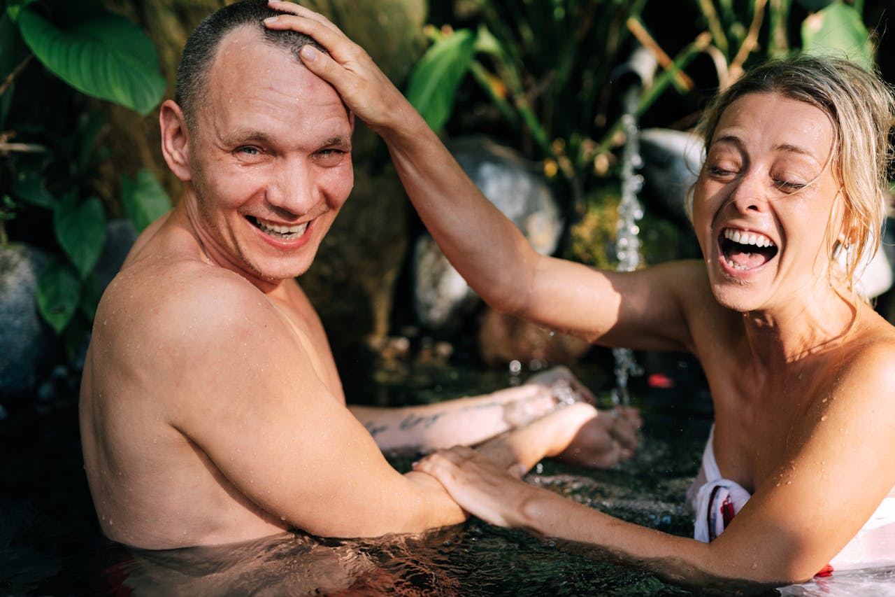 Happy couple laughing and playing in a natural water setting, enjoying a relaxed time together.