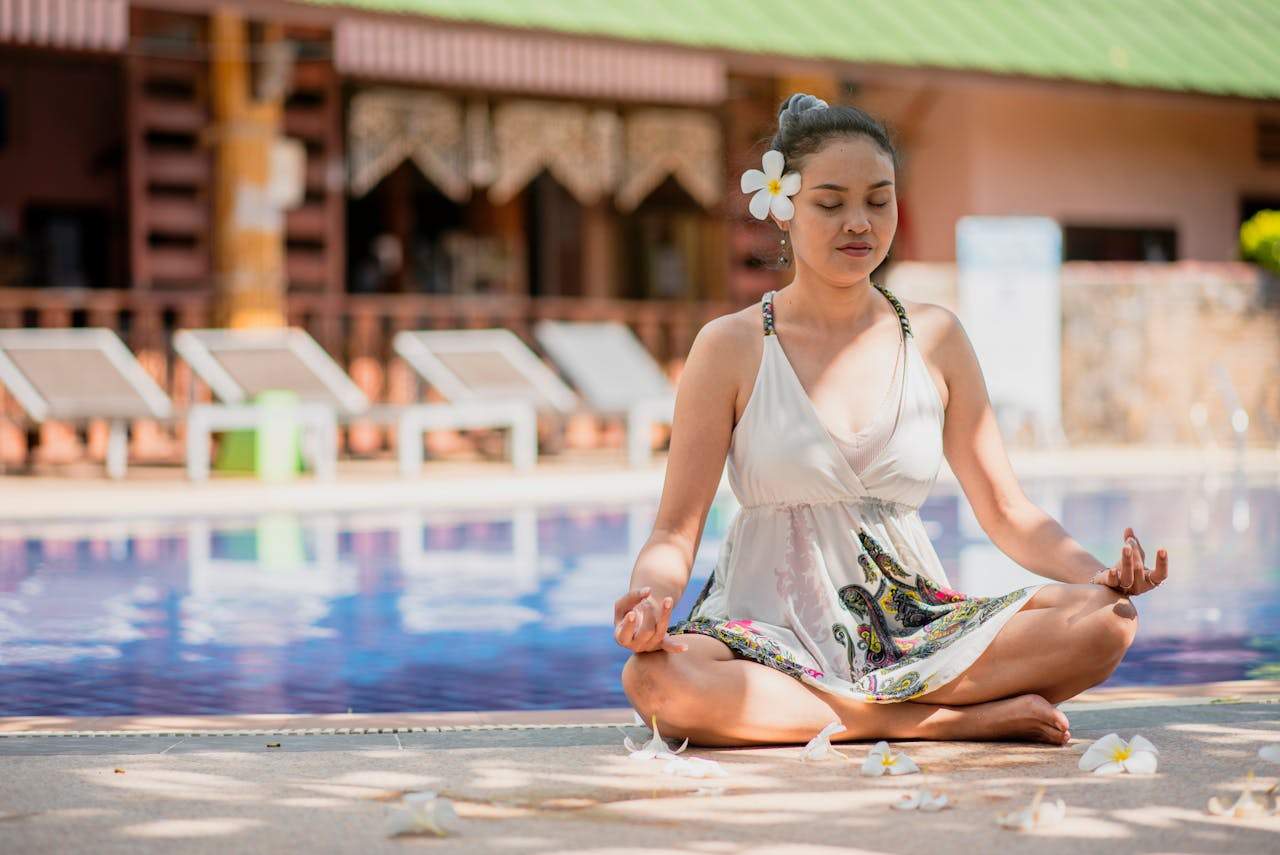 A woman practicing yoga meditation by a pool in summer, embracing relaxation and mindfulness.